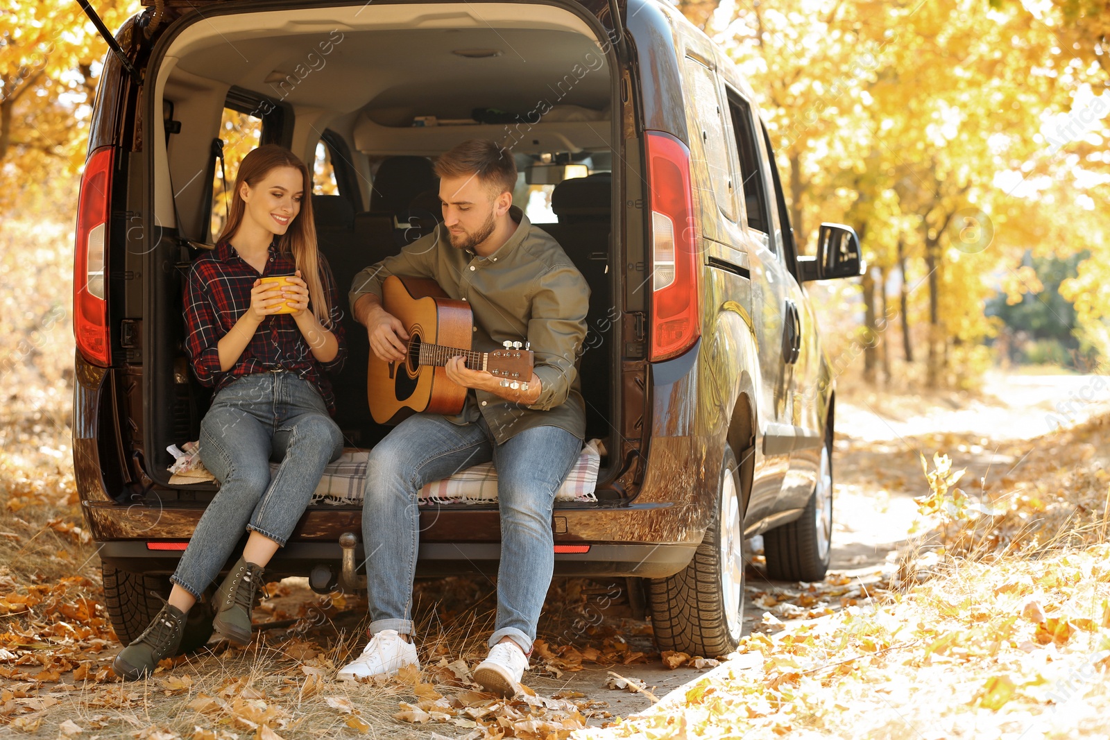 Photo of Young couple with guitar sitting in open car trunk outdoors