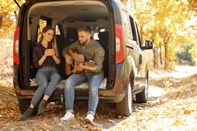 Young couple with guitar sitting in open car trunk outdoors