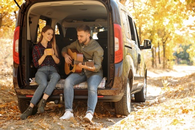 Photo of Young couple with guitar sitting in open car trunk outdoors