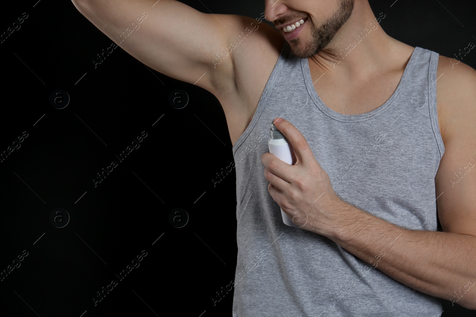 Photo of Man applying deodorant on black background, closeup. Space for text