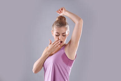 Young woman with sweat stain on her clothes against grey background. Using deodorant