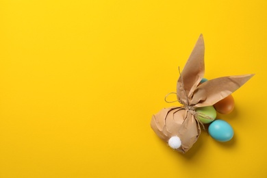 Flat lay composition of Easter bunny gift bag and dyed eggs on color background. Space for text