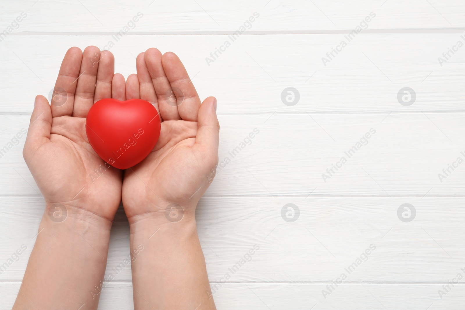 Photo of Man holding red decorative heart on white wooden background, top view and space for text. Cardiology concept