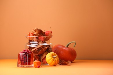 Composition with beautiful autumn leaves, berries and pumpkins on table against orange background, space for text