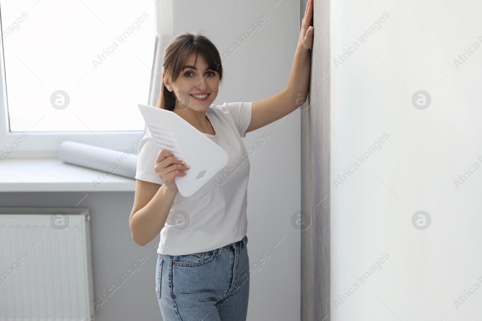 Photo of Woman with spatula hanging stylish gray wallpaper in room