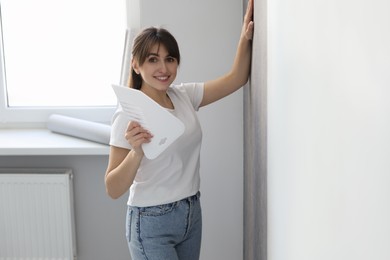 Photo of Woman with spatula hanging stylish gray wallpaper in room