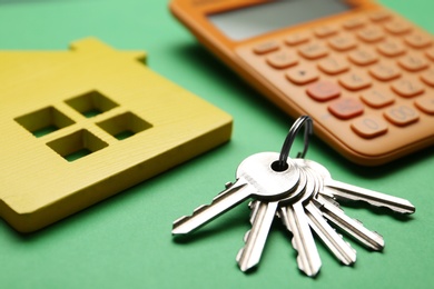 Photo of House figure with calculator and keys on green background, closeup. Real estate agent service
