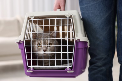 Photo of Travel with pet. Man holding carrier with cute cat at home, closeup