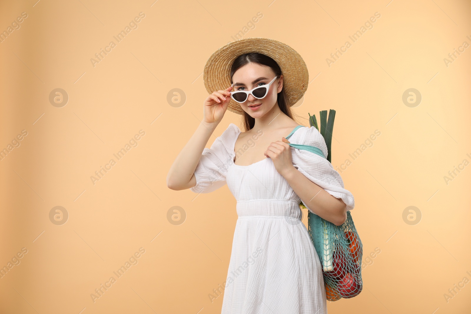 Photo of Woman with string bag of fresh vegetables on beige background, space for text
