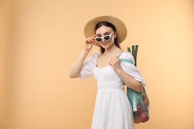 Woman with string bag of fresh vegetables on beige background, space for text