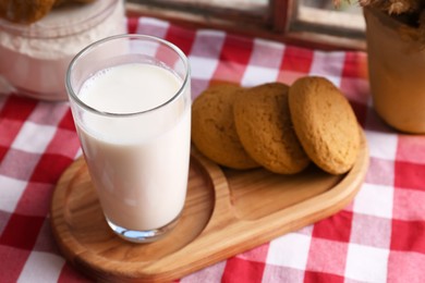 Glass of milk with cookies on red checkered tablecloth, closeup