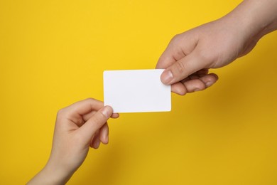 Photo of Man and woman holding blank gift card on yellow background, closeup