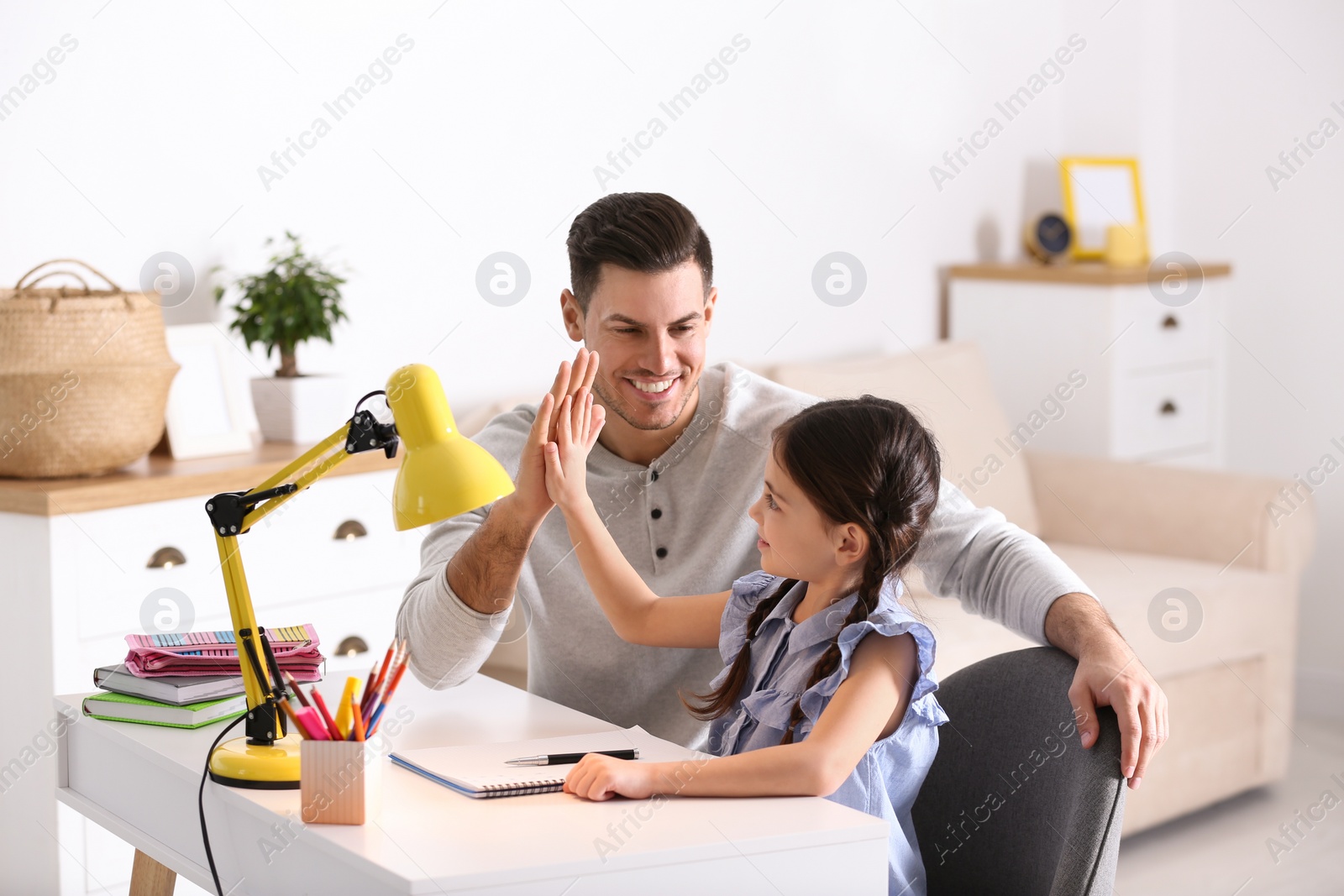 Photo of Father and daughter doing homework together at table indoors