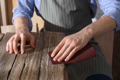 Photo of Man polishing wooden table with sandpaper indoors, closeup