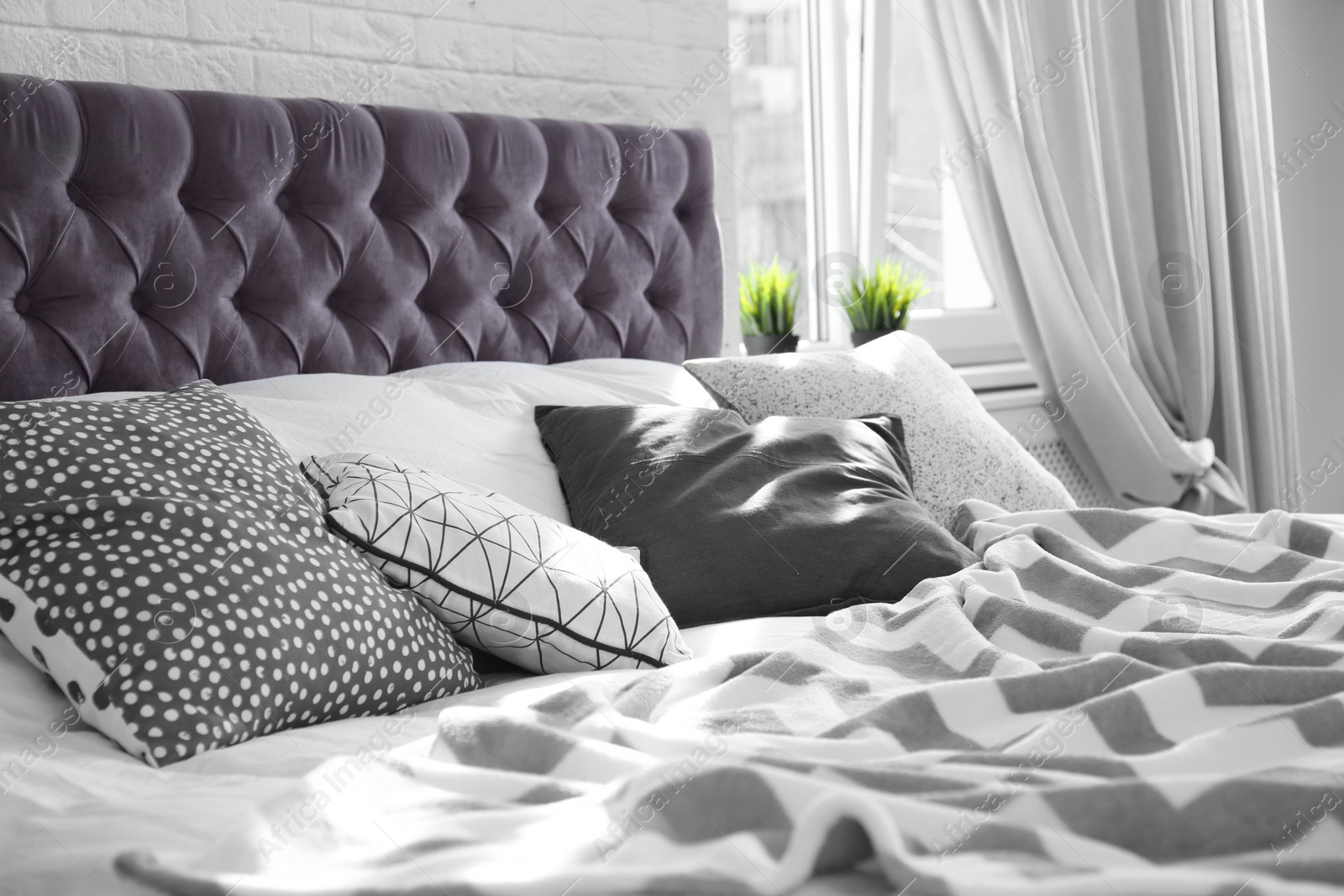 Photo of Bed with pillows and plaid near brick wall. Interior design