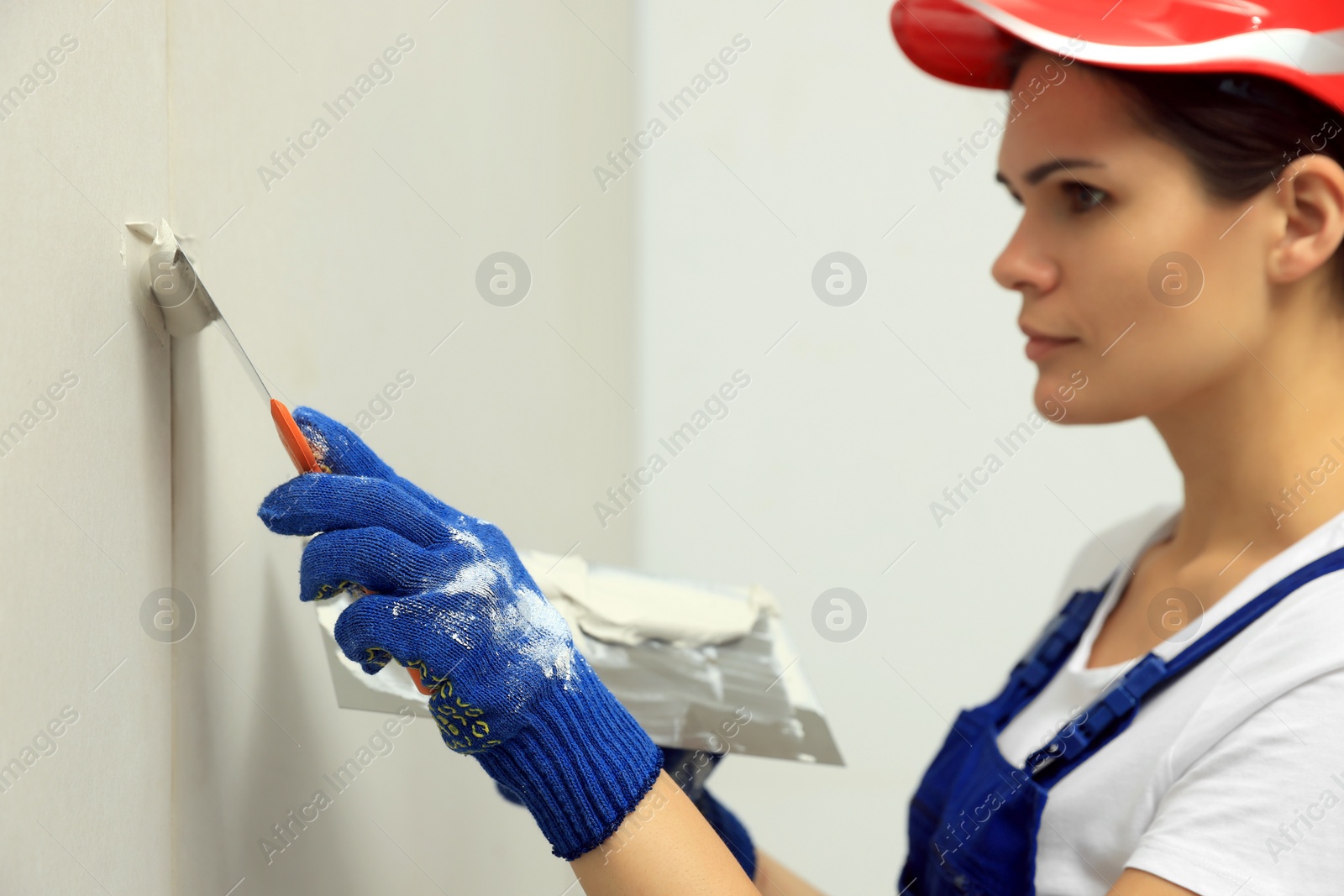 Photo of Professional worker in hard hat plastering wall with putty knives, focus on hand
