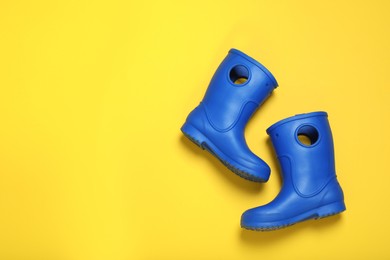Photo of Pair of bright blue rubber boots on yellow background top view. Space for text