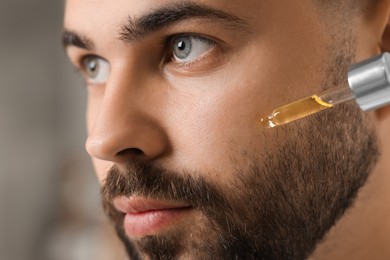 Photo of Handsome man applying cosmetic serum onto his face on blurred background, closeup