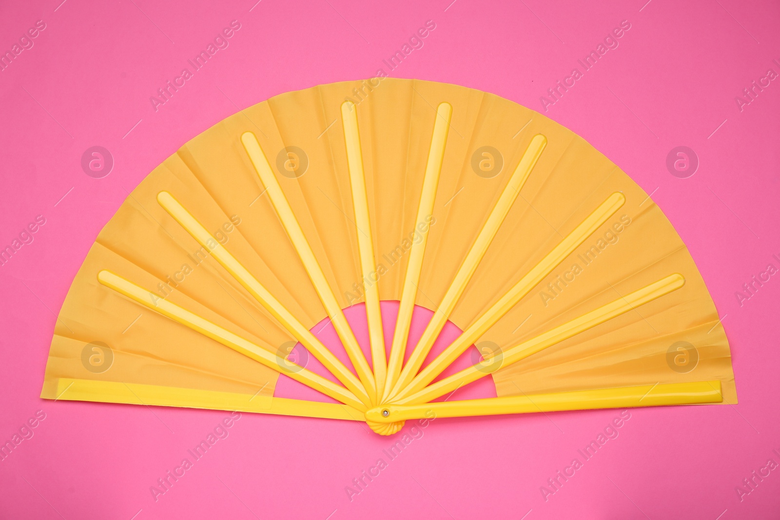 Photo of Bright yellow hand fan on pink background, top view