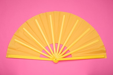 Bright yellow hand fan on pink background, top view