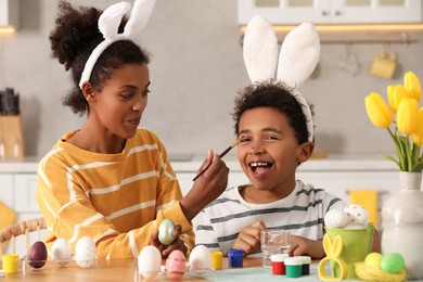 Photo of Happy African American mother and her cute son having fun while painting Easter eggs at table in kitchen