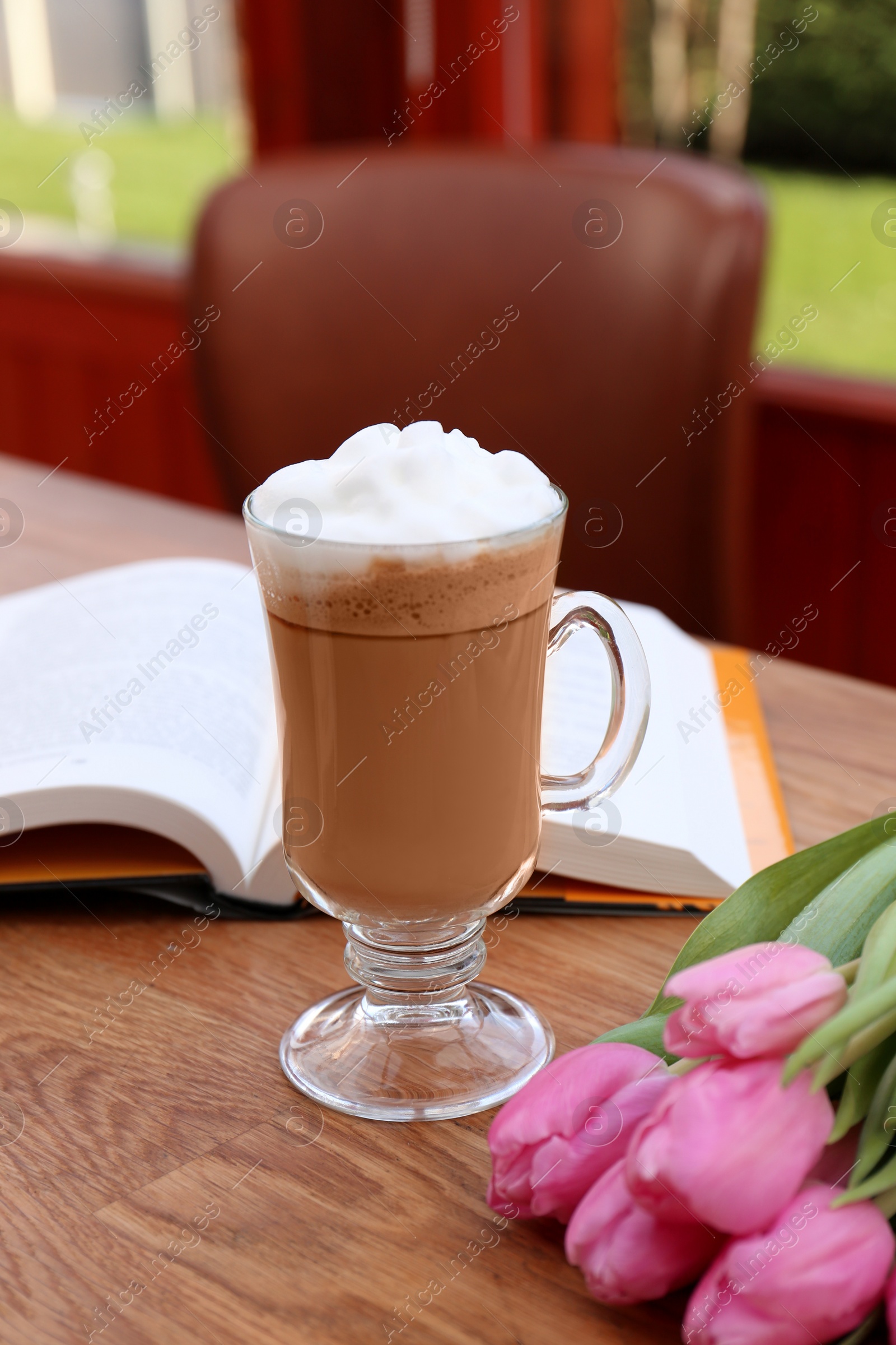 Photo of Glass of delicious cocoa and pink tulips on wooden table at balcony