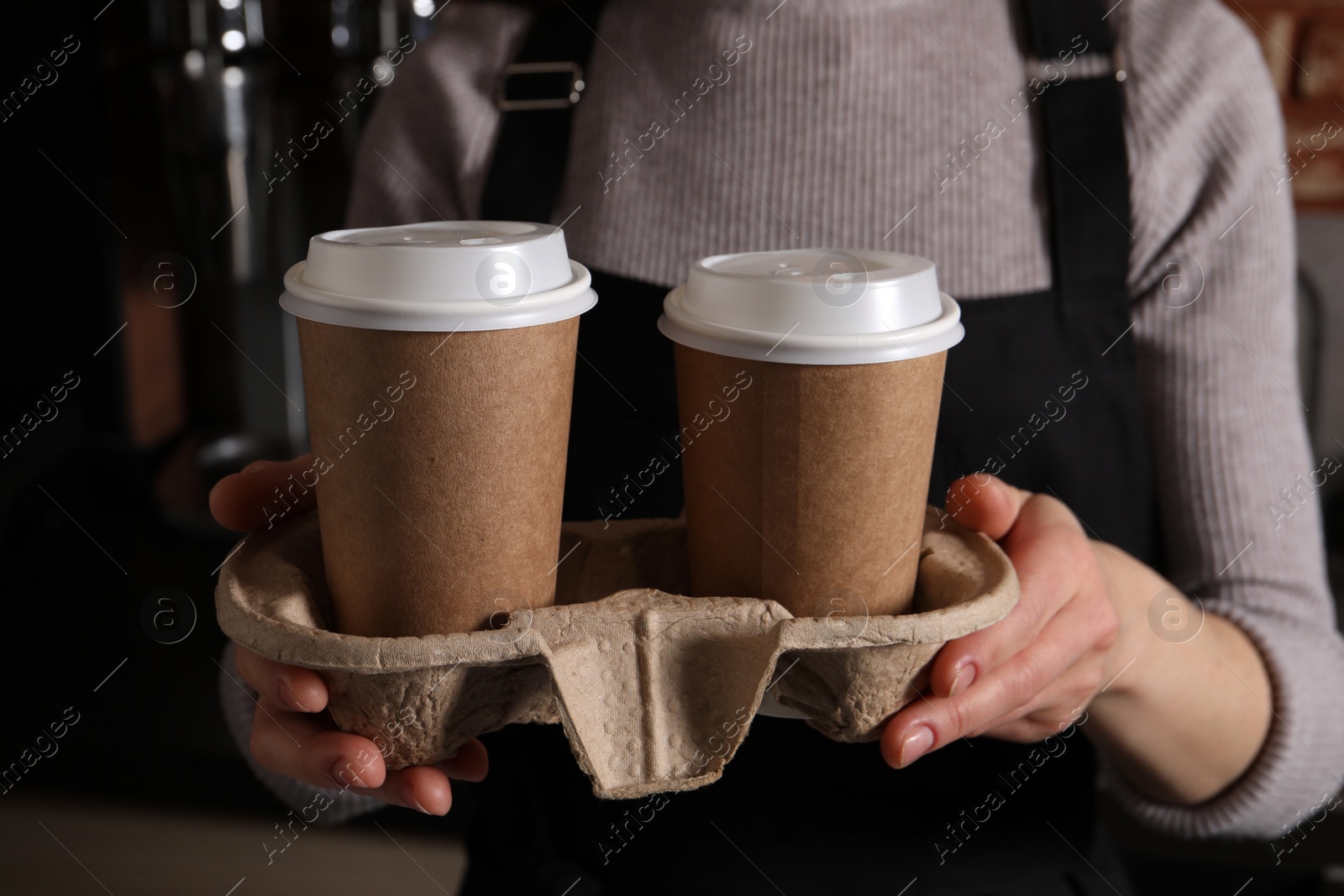 Photo of Barista holding takeaway paper cups with coffee in cafe, closeup