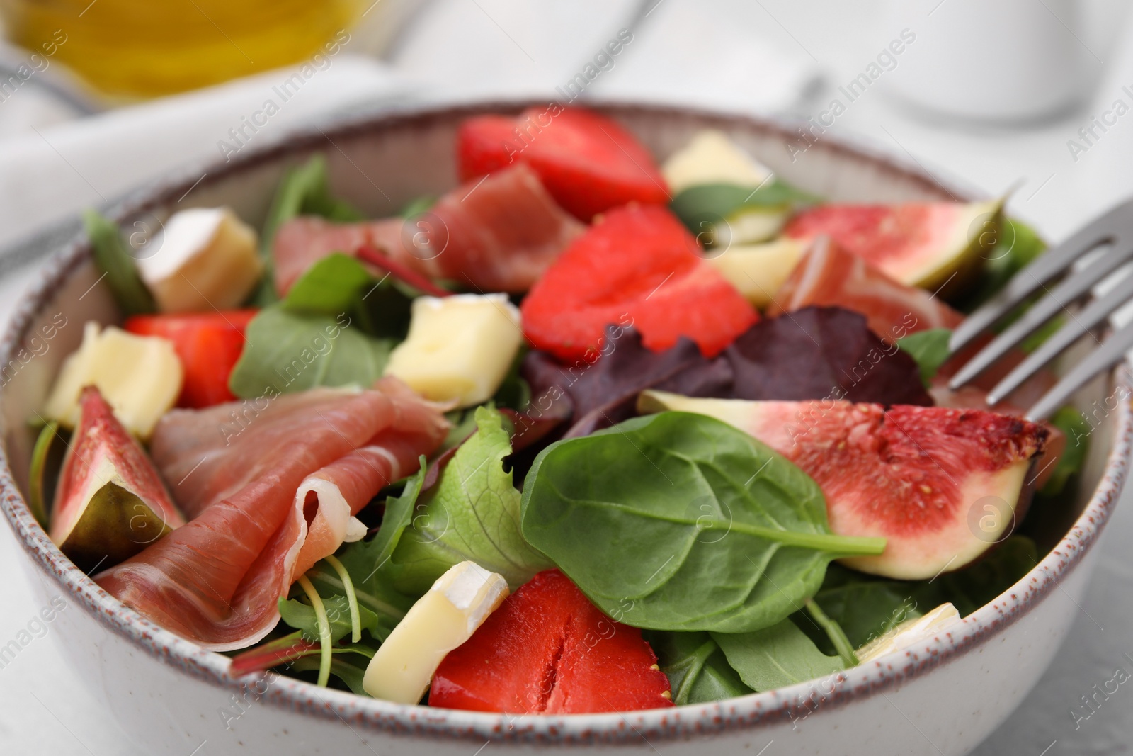 Photo of Tasty salad with brie cheese, prosciutto, strawberries and figs in bowl, closeup