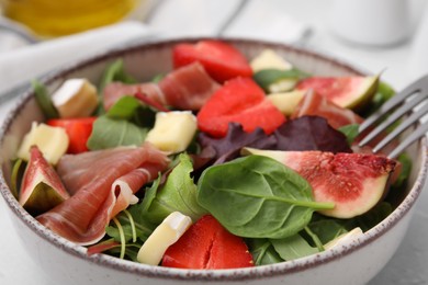 Photo of Tasty salad with brie cheese, prosciutto, strawberries and figs in bowl, closeup