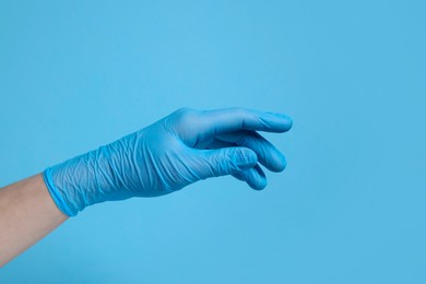 Photo of Doctor wearing medical glove on light blue background, closeup