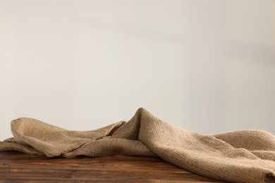 Natural burlap fabric on wooden table against light background. Space for text