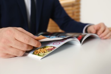Photo of Businessman reading modern magazine at table indoors, closeup