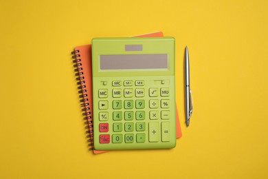 Calculator, notebook and pen on yellow background, flat lay