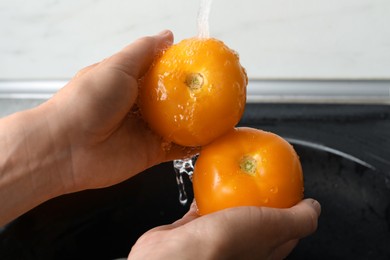 Photo of Woman washing fresh ripe yellow tomatoes, closeup