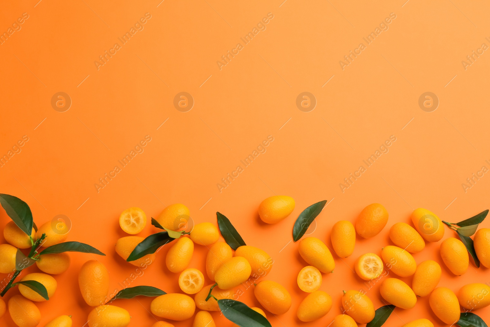 Photo of Fresh ripe kumquats with green leaves on orange background, flat lay. Space for text