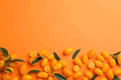 Photo of Fresh ripe kumquats with green leaves on orange background, flat lay. Space for text