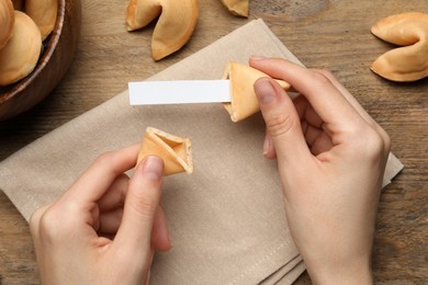 Photo of Woman holding tasty fortune cookie and paper with prediction at wooden table, top view. Space for text