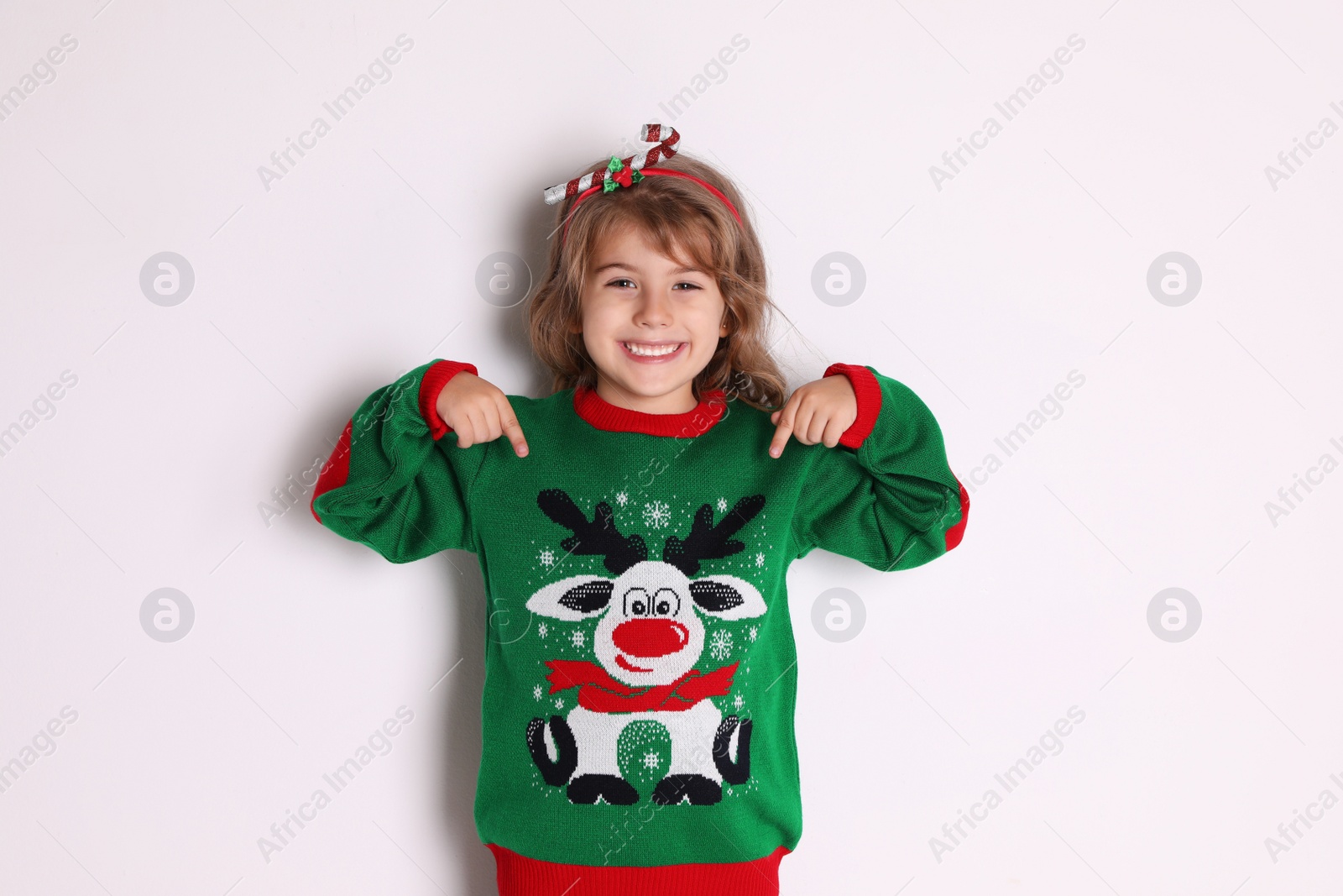 Photo of Cute little girl pointing at her green Christmas sweater against white background