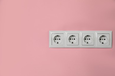 Power sockets on pink wall, space for text. Electrical supply