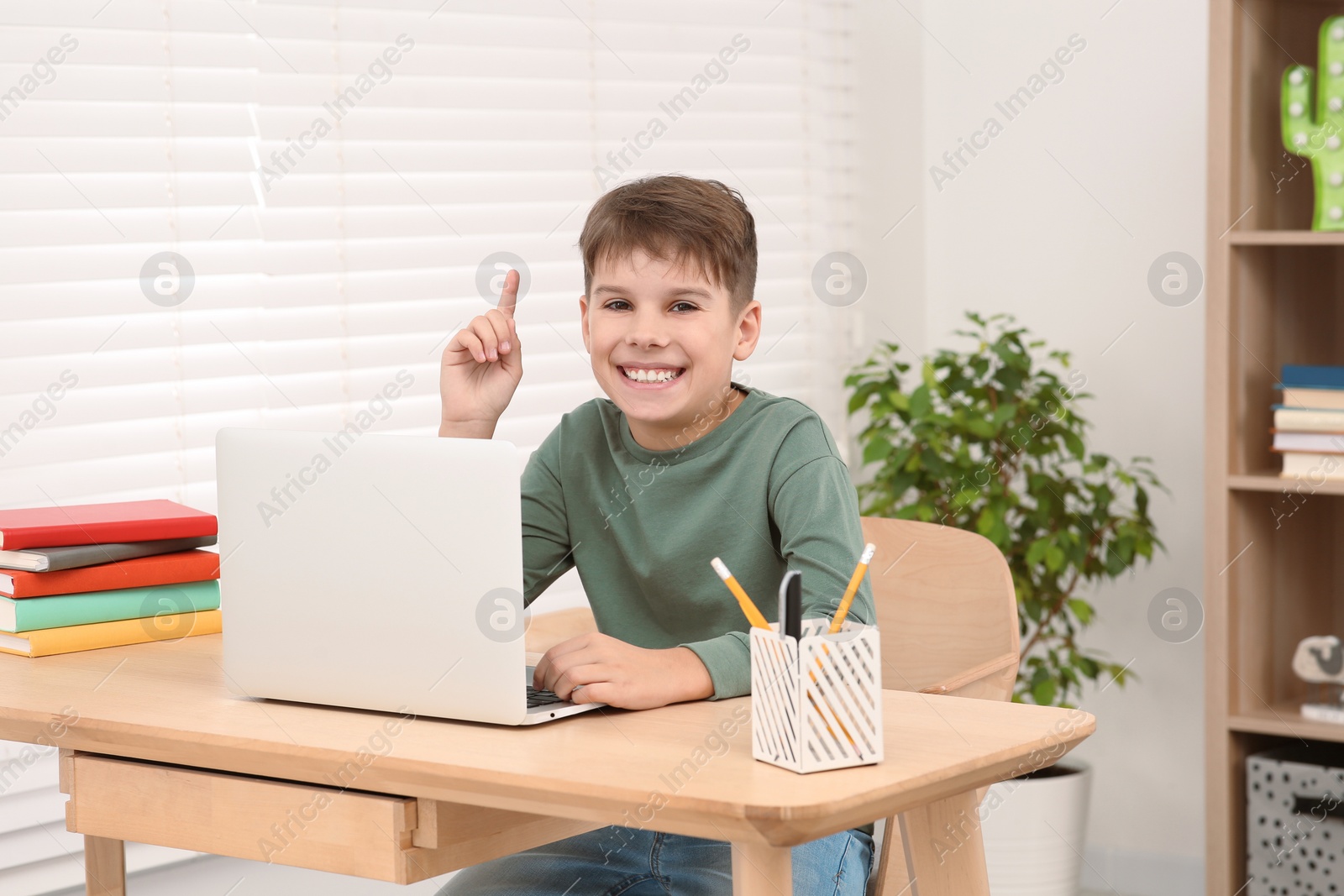 Photo of Boy using laptop at desk in room. Home workplace