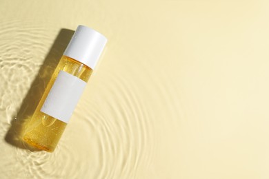 Bottle of cosmetic oil in water on beige background, top view. Space for text