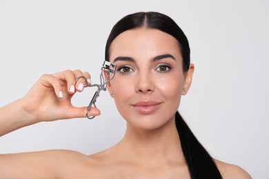 Beautiful young woman using eyelash curler on white background