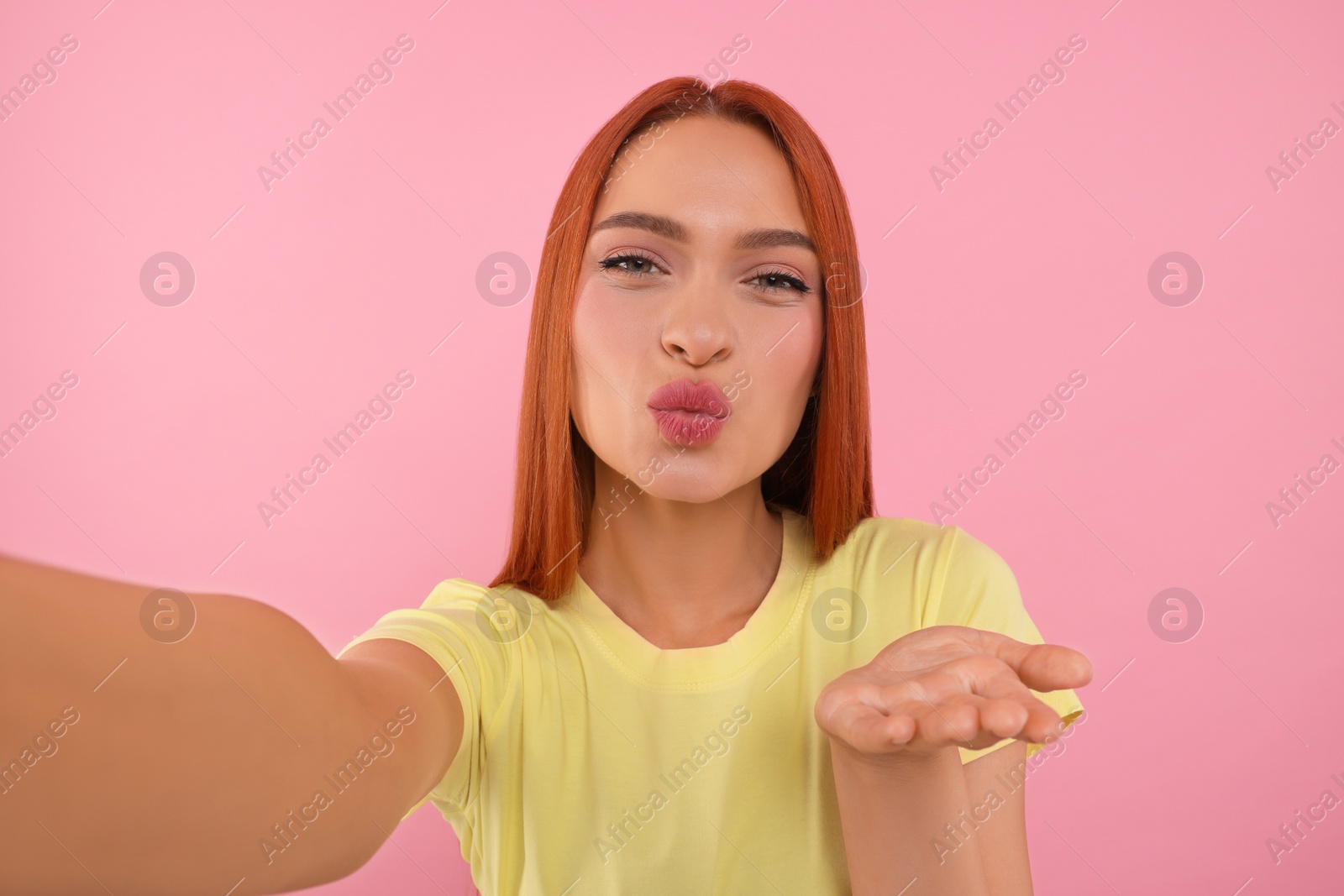 Photo of Beautiful woman taking selfie and blowing kiss on pink background