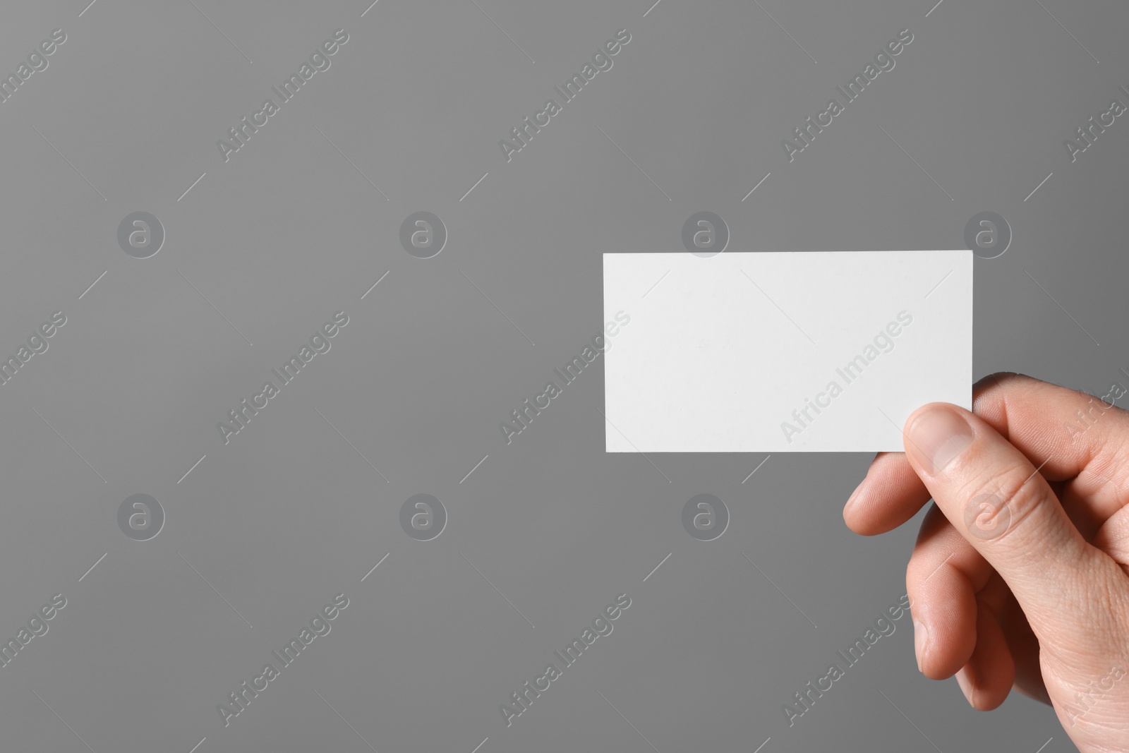 Photo of Man holding blank business card on grey background, closeup. Space for text