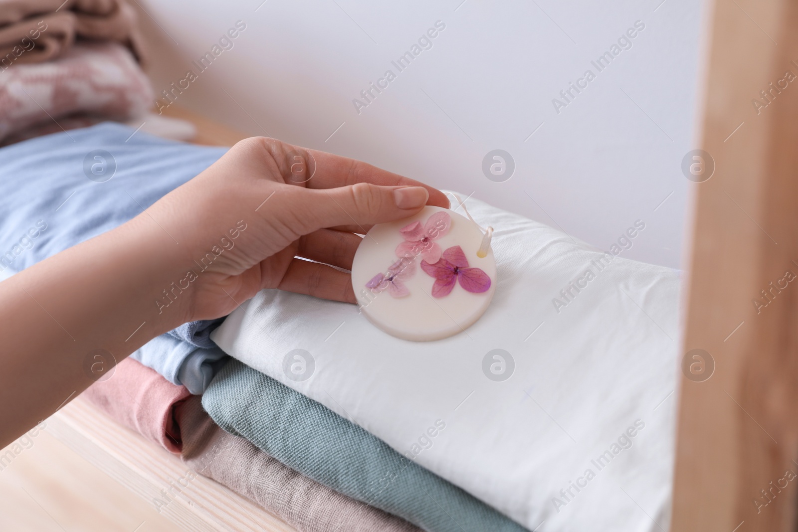 Photo of Woman putting scented wax sachet onto stack of clothes indoors, closeup