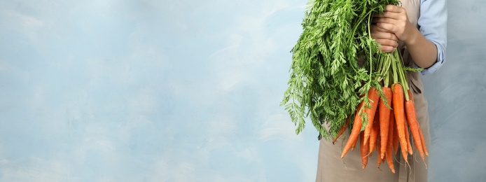 Image of Woman holding fresh ripe carrots against light blue background, closeup with space for text. Banner design 