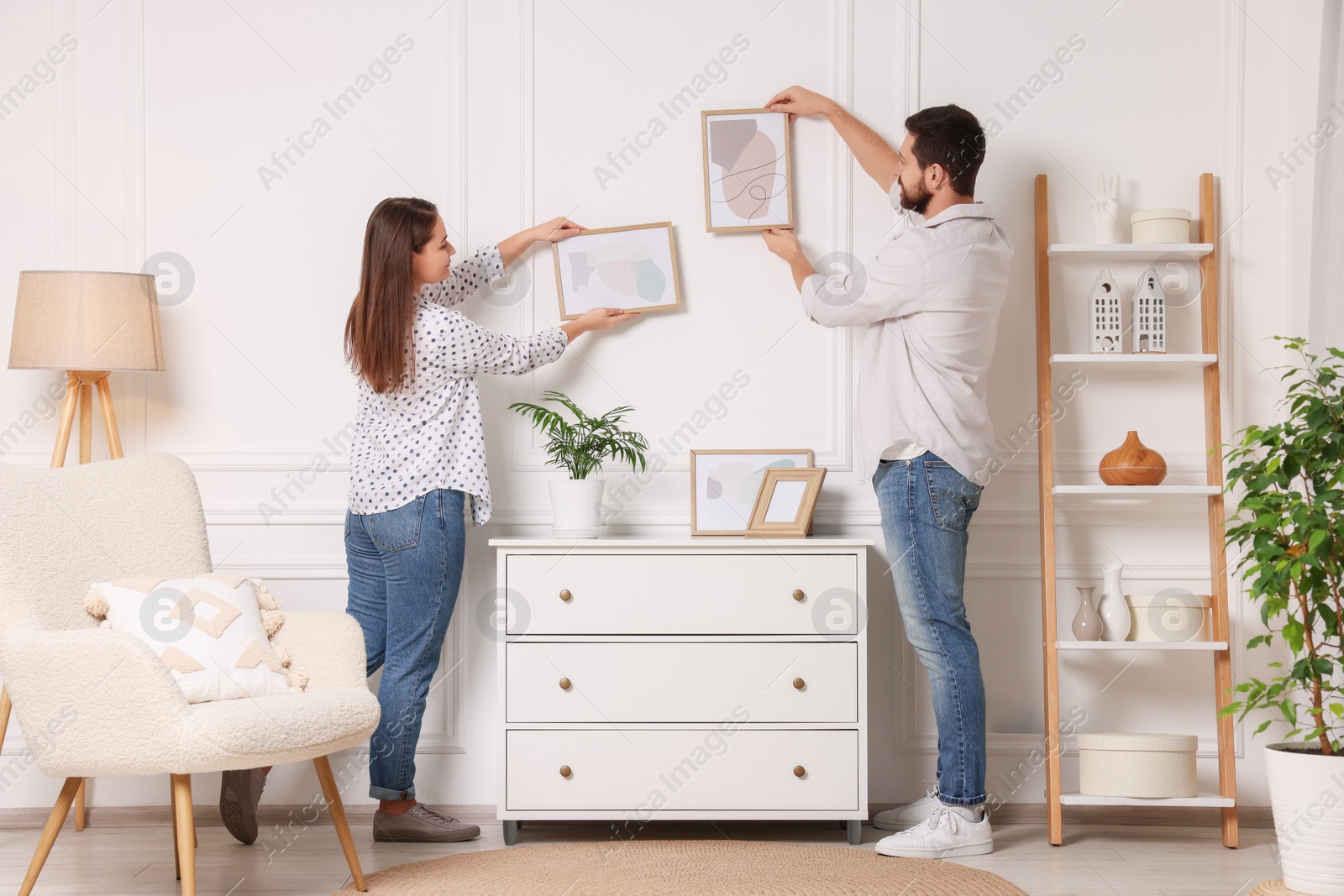 Photo of Man and woman hanging picture frames on white wall at home