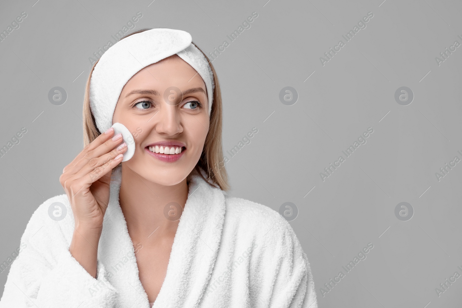 Photo of Young woman cleaning face with cotton pad on light grey background. Space for text