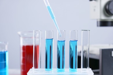 Photo of Dripping liquid from pipette into test tube on blurred background, closeup