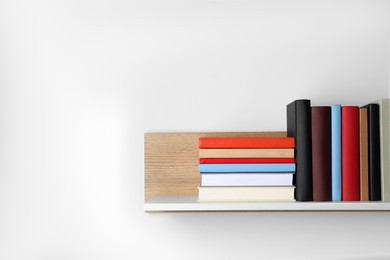 Photo of Many hardcover books on wooden shelf near white wall. Space for text